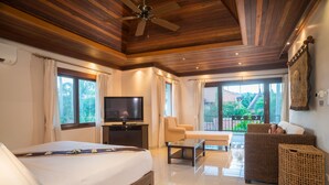 Une pièce spacieuse avec un grand lit, une télévision, un canapé et un balcon offrant une vue sur la verdure.