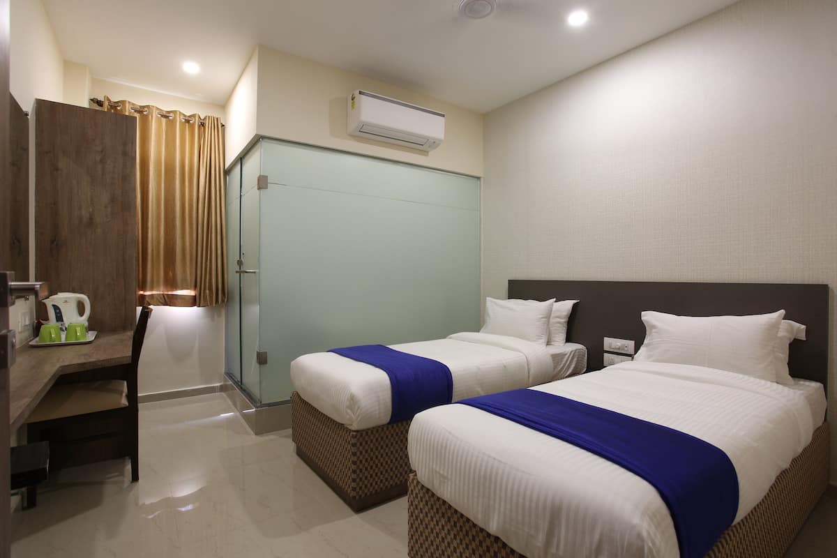 A hotel room with two beds, a desk with a chair, a coffee maker, and a wardrobe.