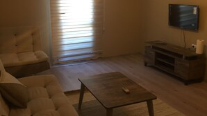 Una sala de estar con un sofá, una mesa de centro, un televisor y una ventana con persianas.