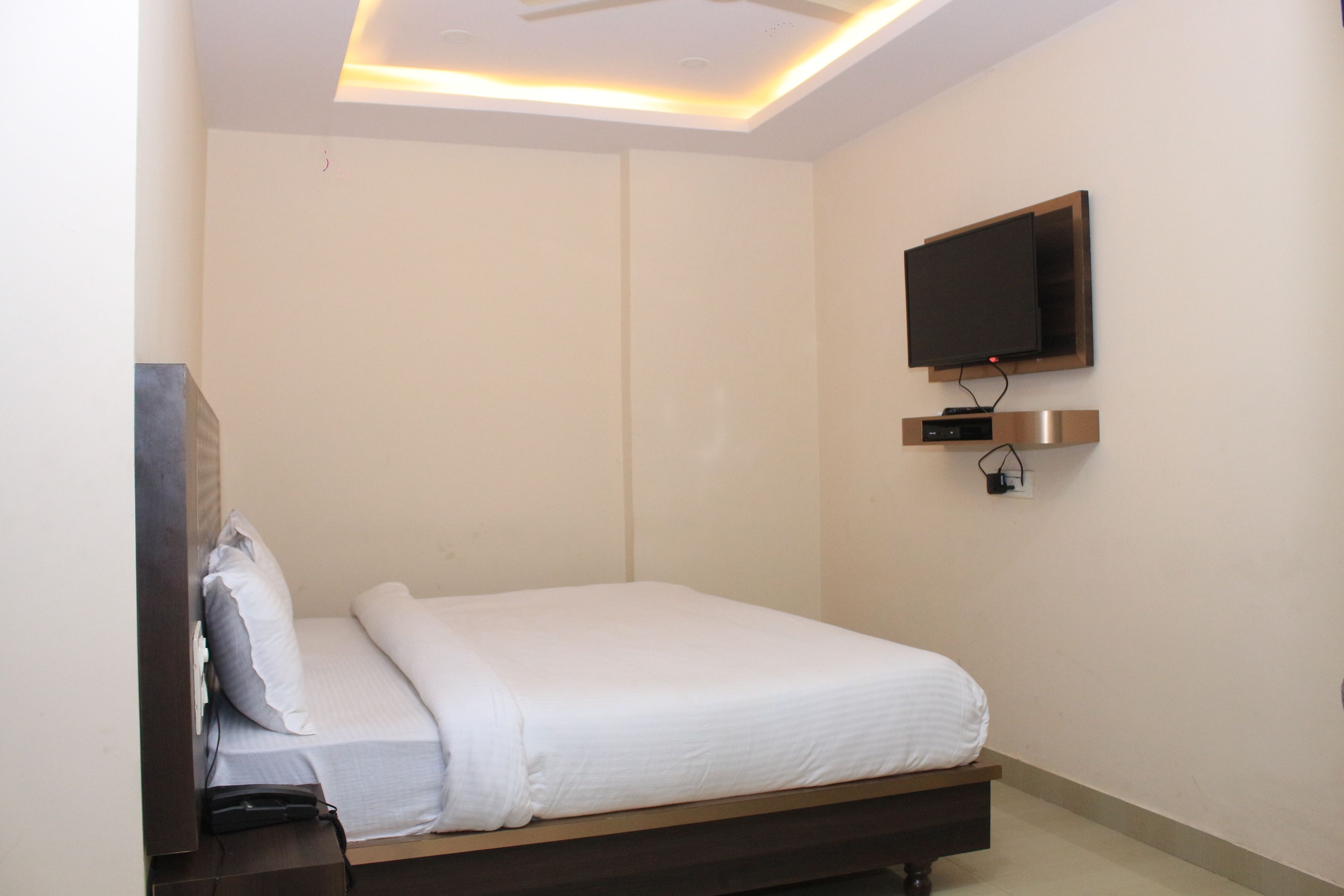 Een slaapkamer met een bed, een aan de muur bevestigde televisie en een plafondlamp.