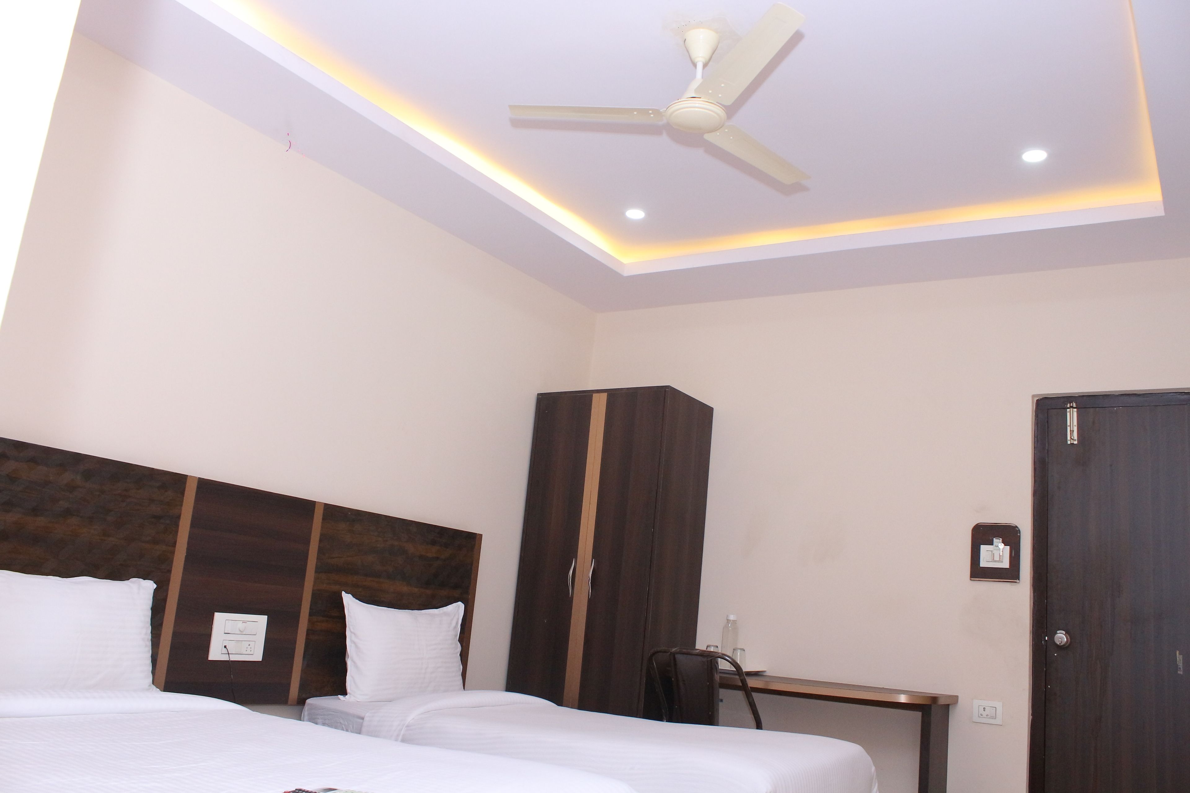 A hotel room with two beds, a ceiling fan, a wardrobe, and a desk.