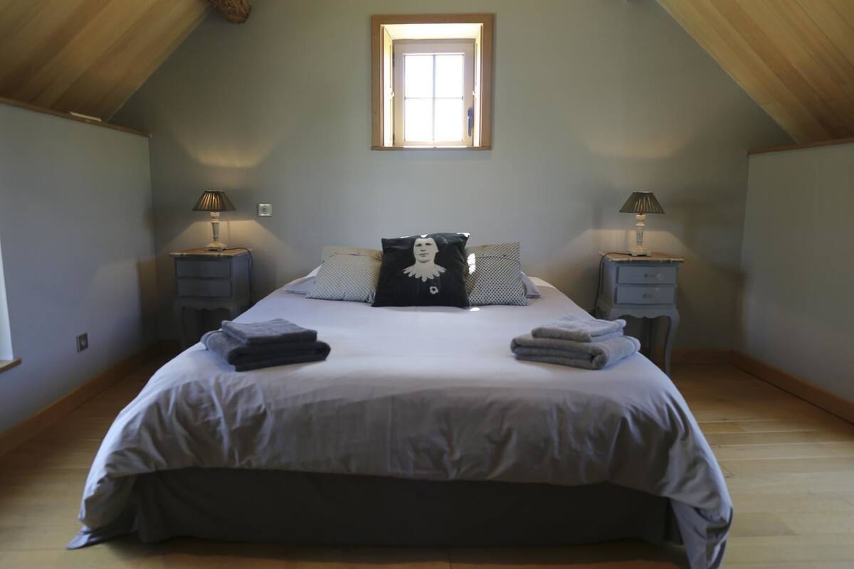 A bedroom with a large bed, two bedside tables with lamps, a window, and a wooden ceiling.