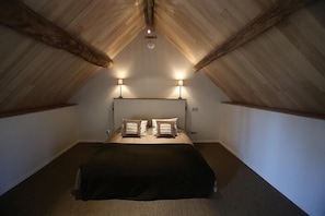 A bedroom with a sloped ceiling, two bedside lamps, a bed with a dark cover, and a headboard.