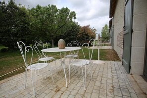 A patio area with a white metal table and chairs, a decorative stone, and a brick wall.