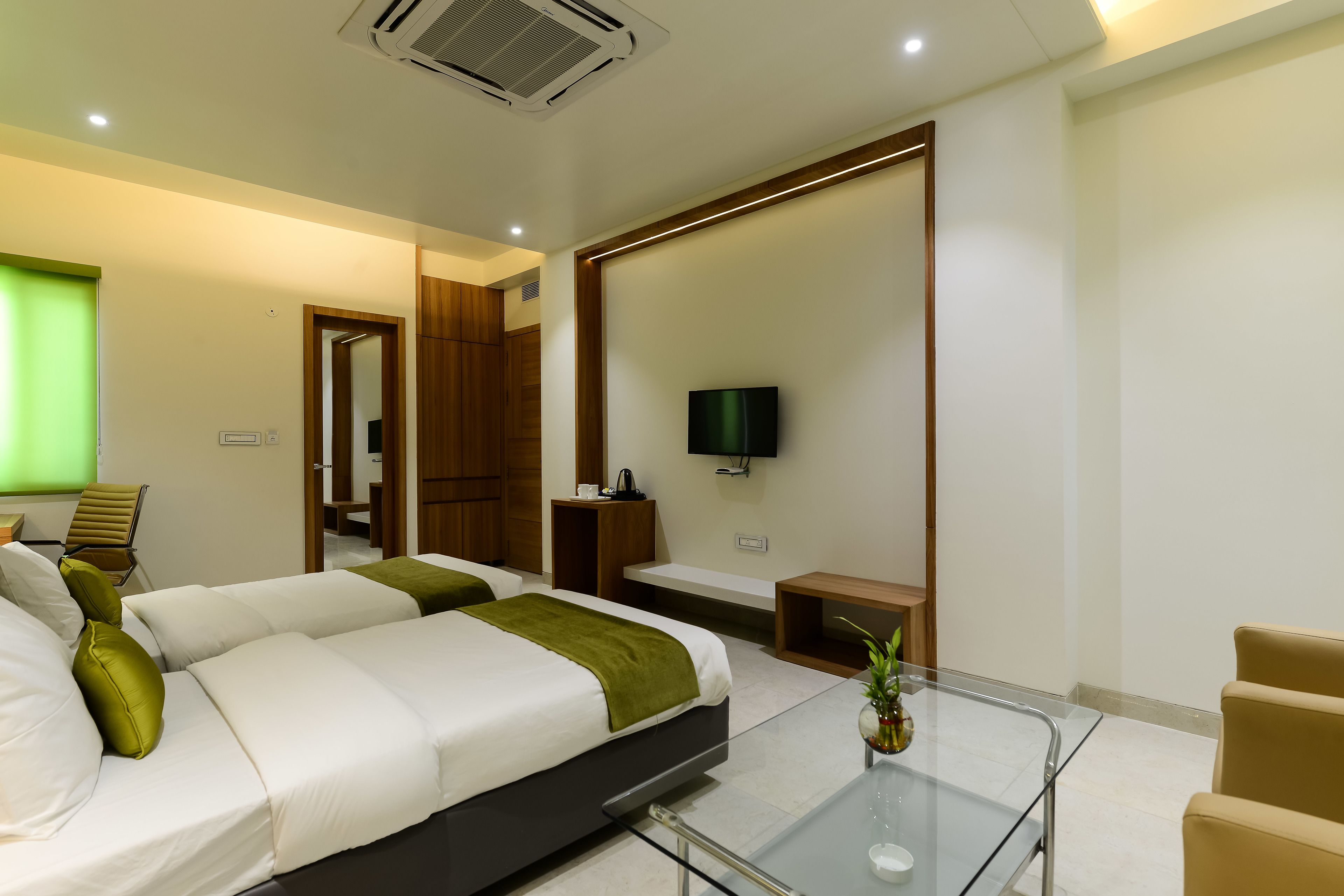 A modern hotel room with a large bed, a glass coffee table, a TV, and a seating area with chairs.