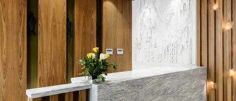 Un mostrador de recepción con encimera de mármol, paneles de madera e iluminación empotrada.