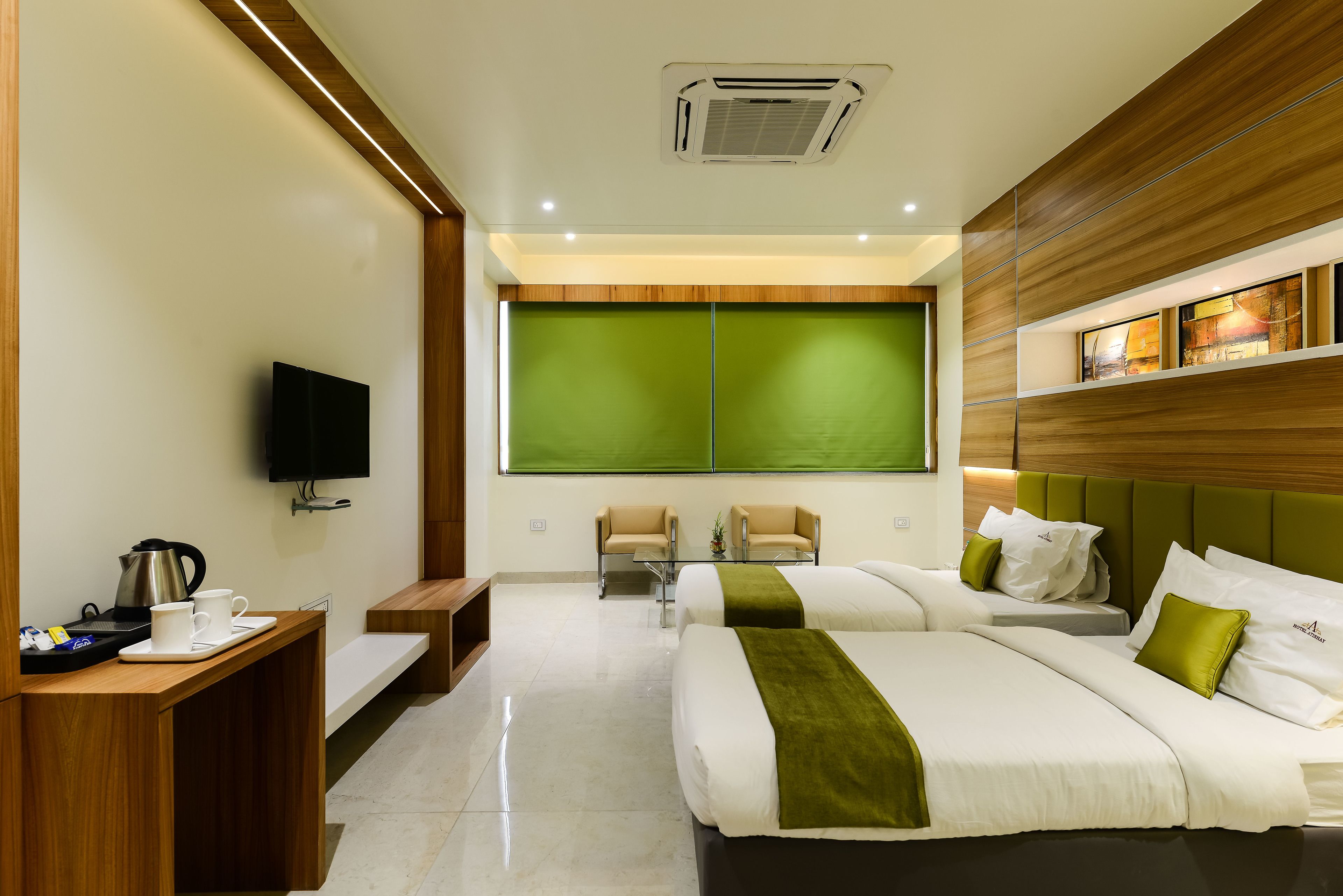 Habitación de hotel con dos camas, un televisor, un escritorio con hervidor y una pared verde.