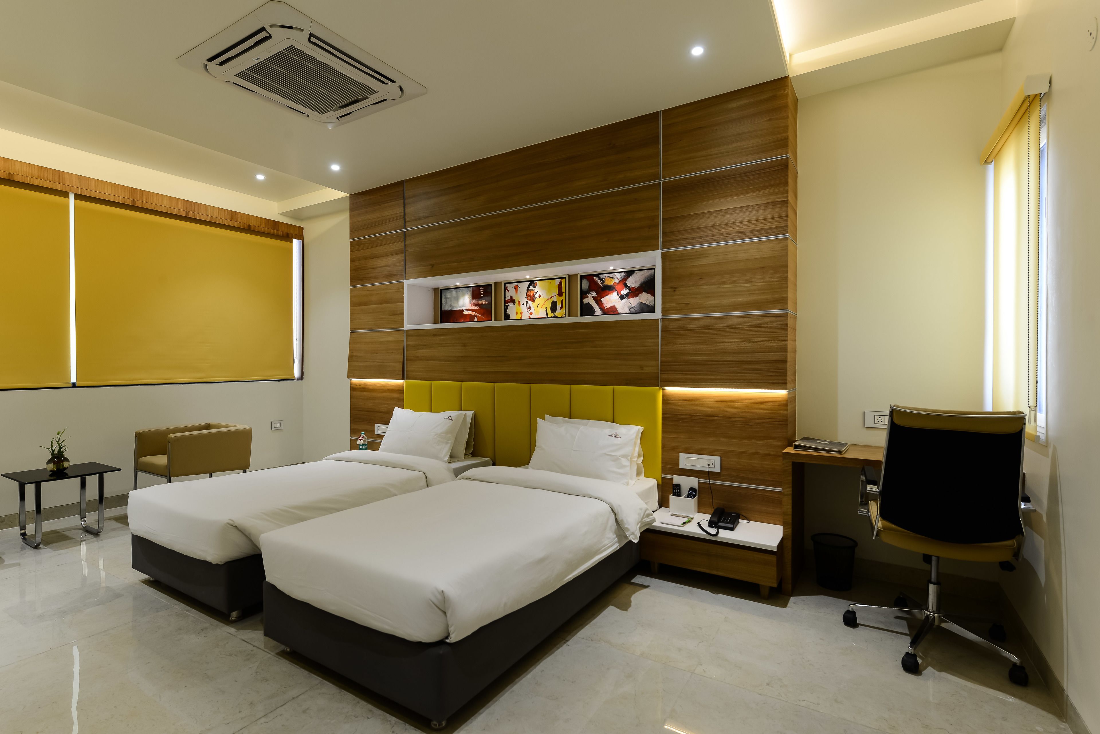 A hotel room with two beds, a desk, a chair, and a TV.
