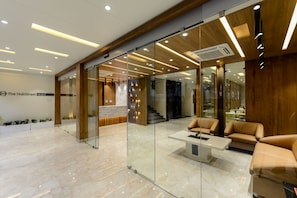 A modern hotel lobby with glass walls, a reception desk, leather seating, and a marble floor.