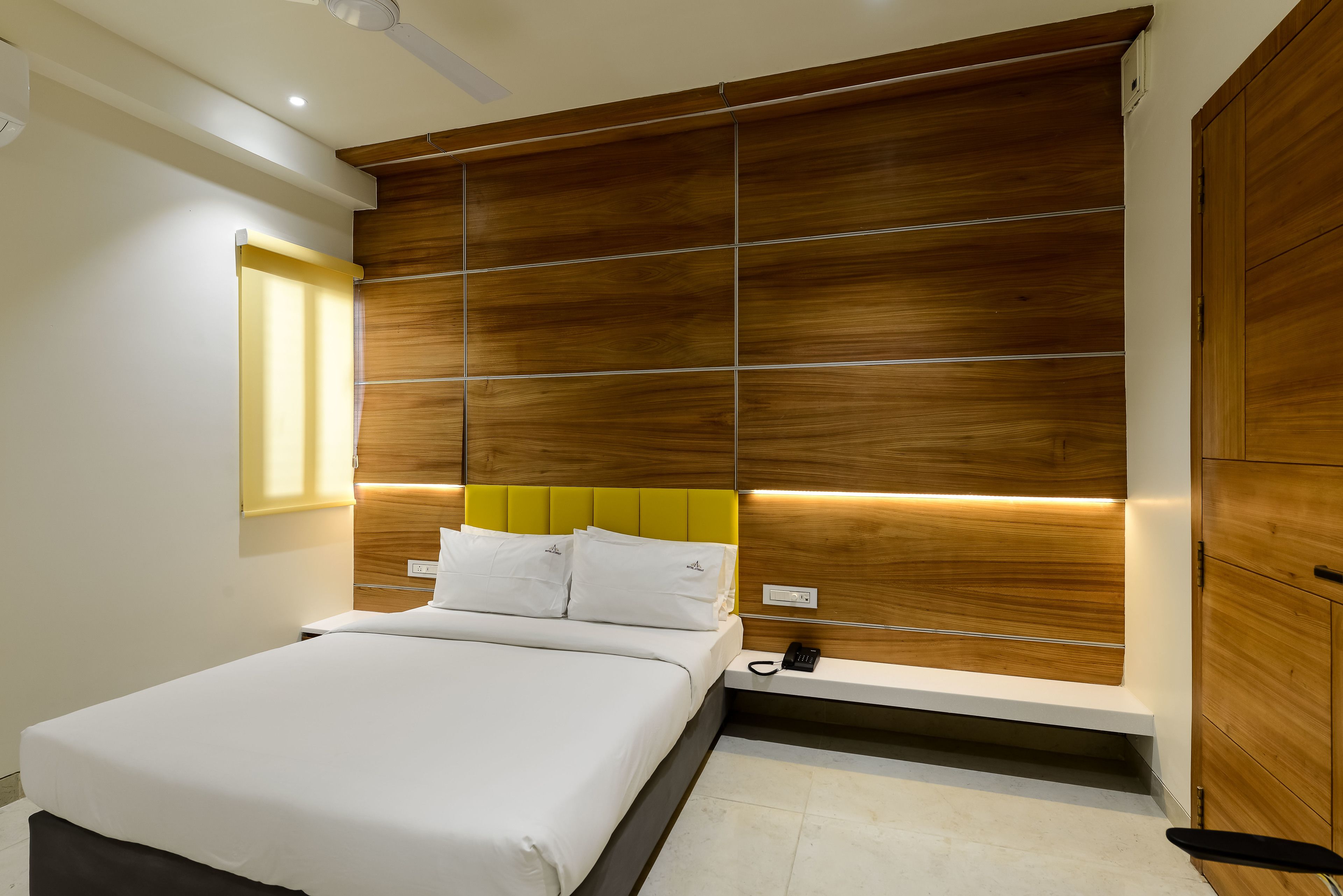 A modern bedroom with a large bed, a wooden headboard, and a bedside table with a phone.