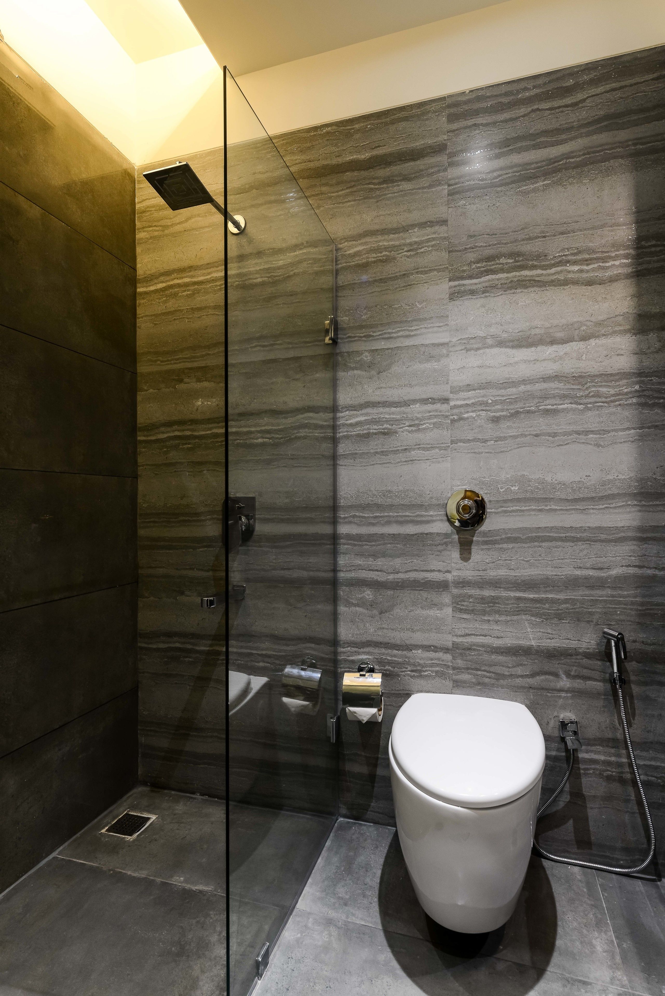 A modern bathroom with a glass-enclosed shower, a white toilet, and a marble-patterned wall.
