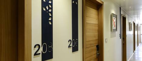 A hotel corridor with wooden doors, numbered room signs, and a modern light fixture.