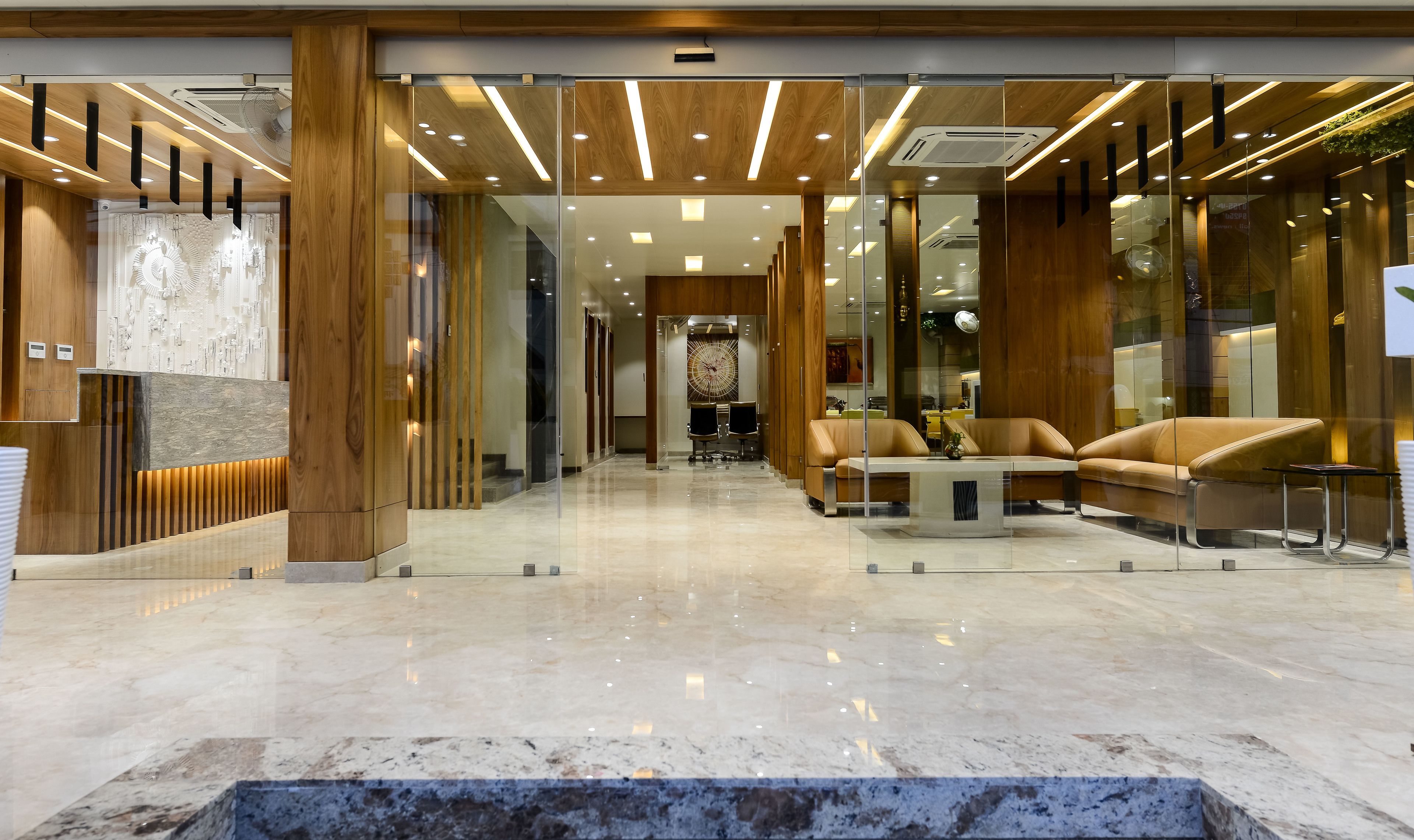 A modern lobby with a reception desk, seating area, and a glass partition.