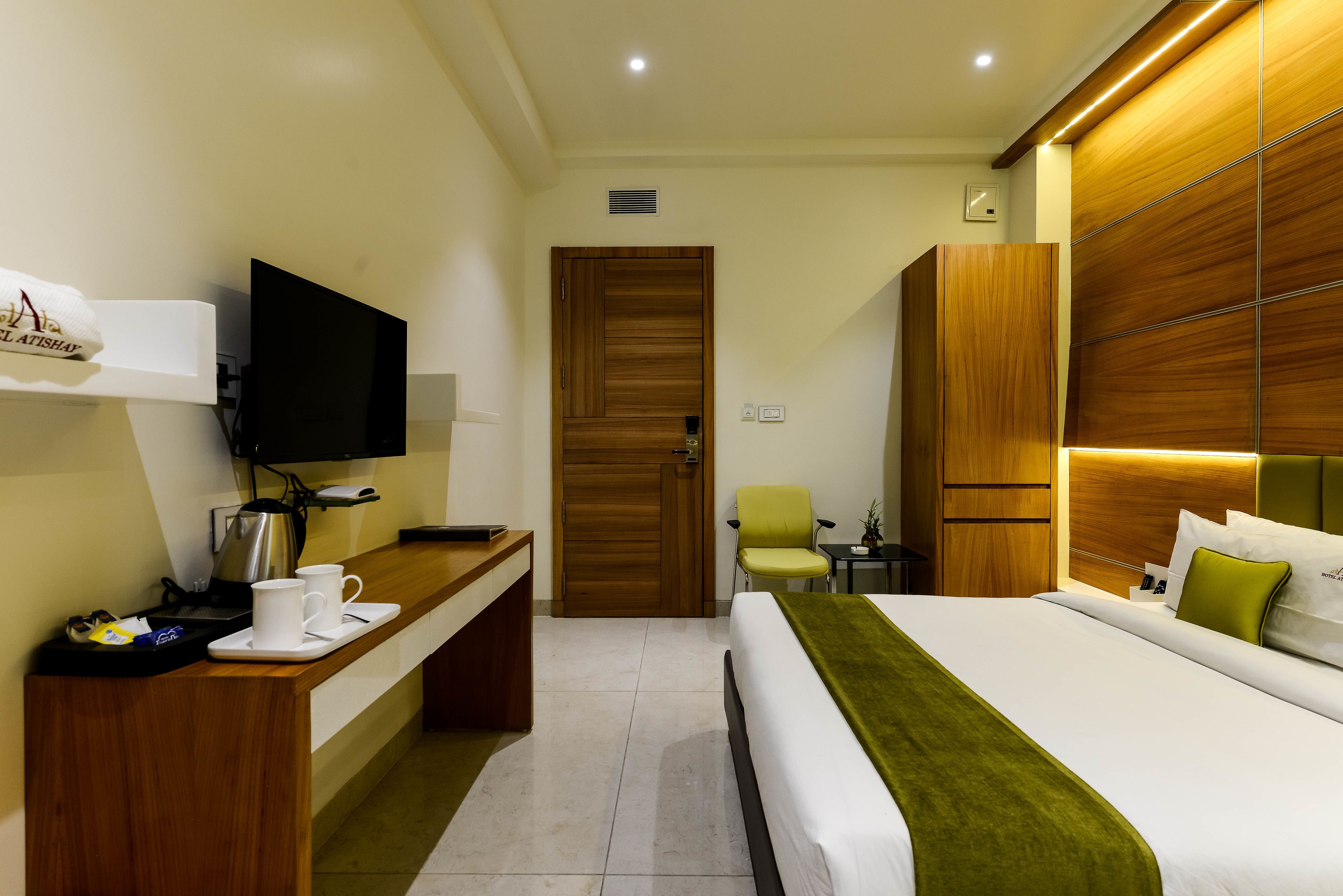 A hotel room with a bed, a desk with a TV, a chair, and a wooden wardrobe.