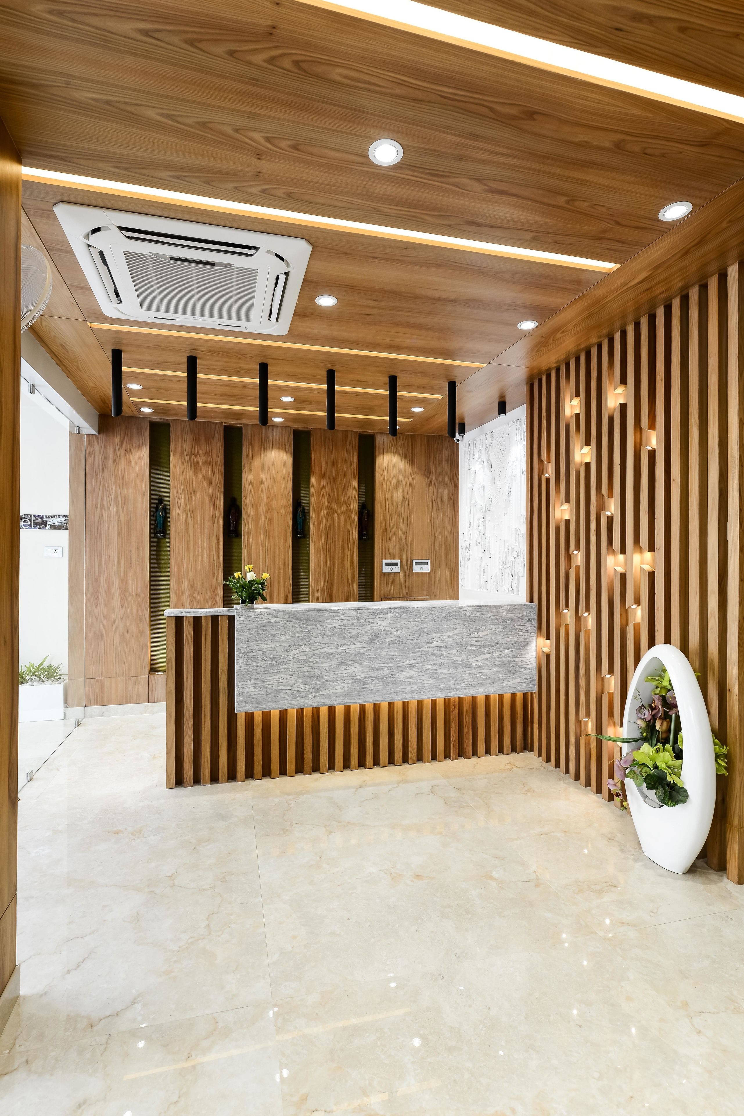 A reception area with a wooden reception desk, a marble floor, and a modern ceiling design with recessed lighting.
