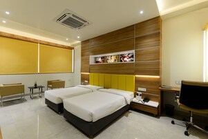 Habitación de hotel con dos camas, un escritorio, una silla, un televisor y un estante con obras de arte.