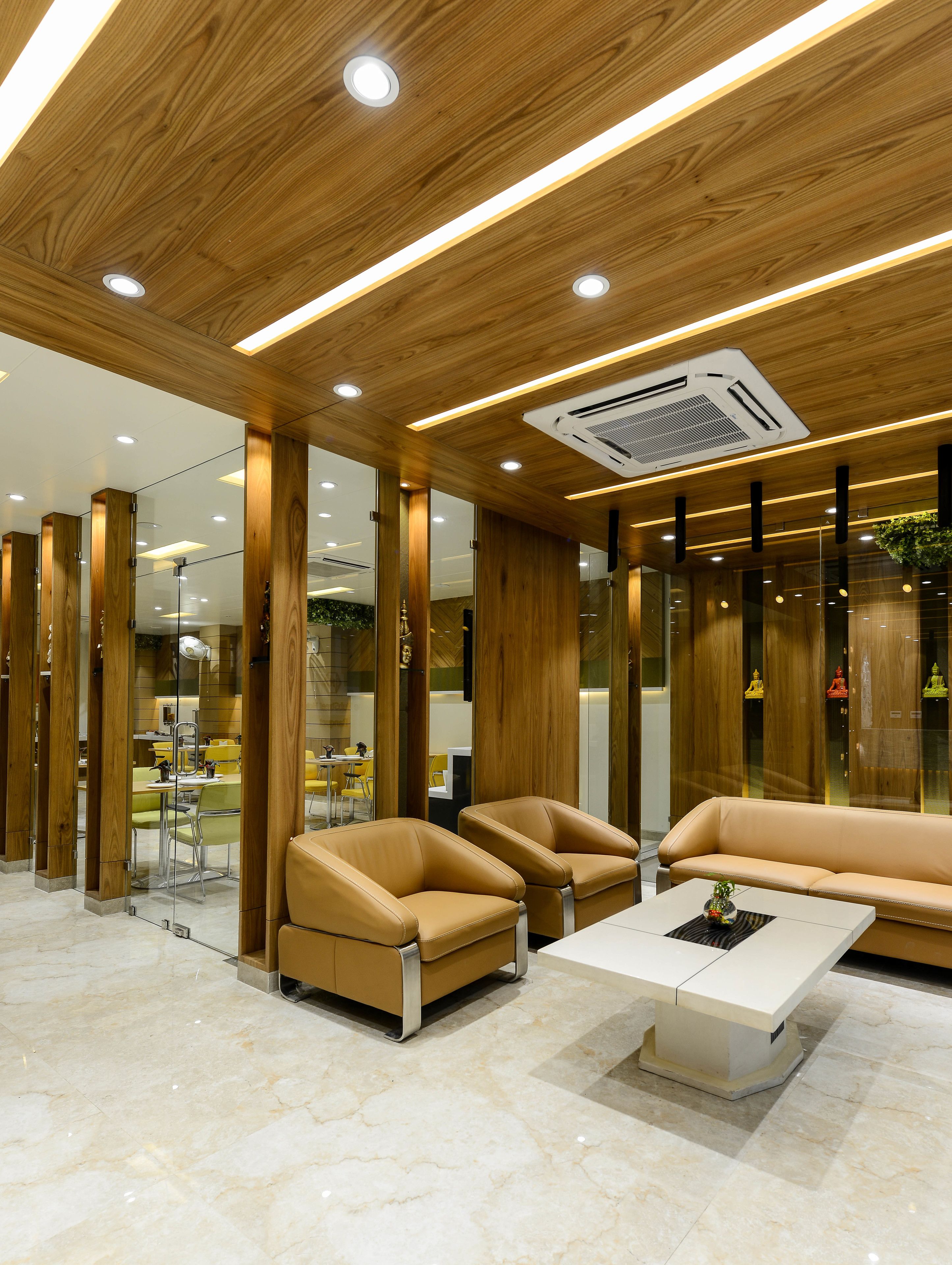 Un hall d’entrée moderne avec des panneaux de plafond en bois, un éclairage encastré, un système de climatisation central et des espaces de détente dotés d’un sol en marbre.
