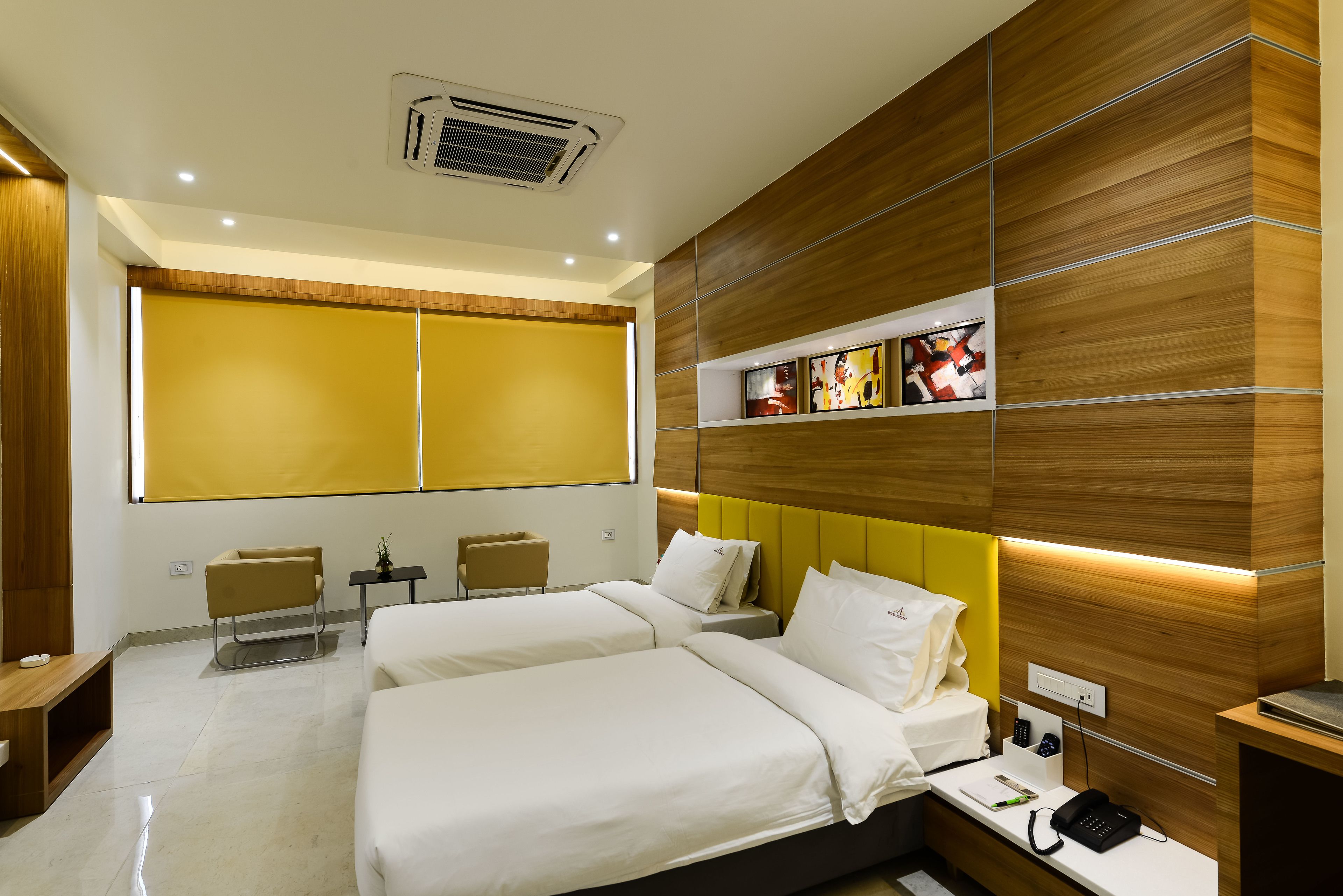 A modern hotel room with two beds, a small table, a chair, and a large window with blinds.
