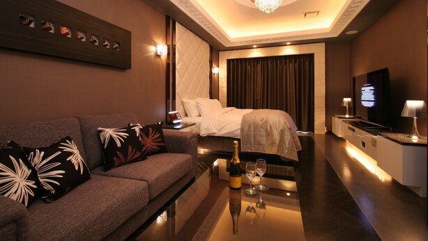 A modern hotel room with a sofa, a bed, a minibar, a TV, and a chandelier. - HOTEL W - Adults Only (Koshigaya)