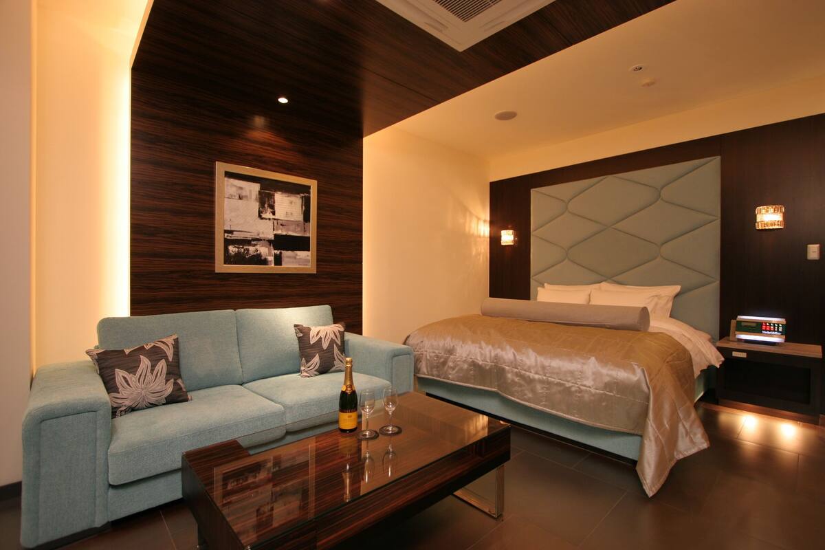 A modern hotel room with a bed, a sofa, a coffee table, and a wall-mounted artwork.