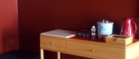 A small wooden desk with a notebook, a thermos, and a kettle.