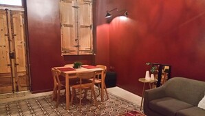 A room with a dining table, chairs, a sofa, a small side table, and a patterned floor. - Squadron Base (Luqa)