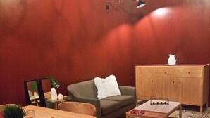 A cozy living room with a wooden dining table, a green sofa, a wooden cabinet, and a patterned floor. - Squadron Base (Luqa)