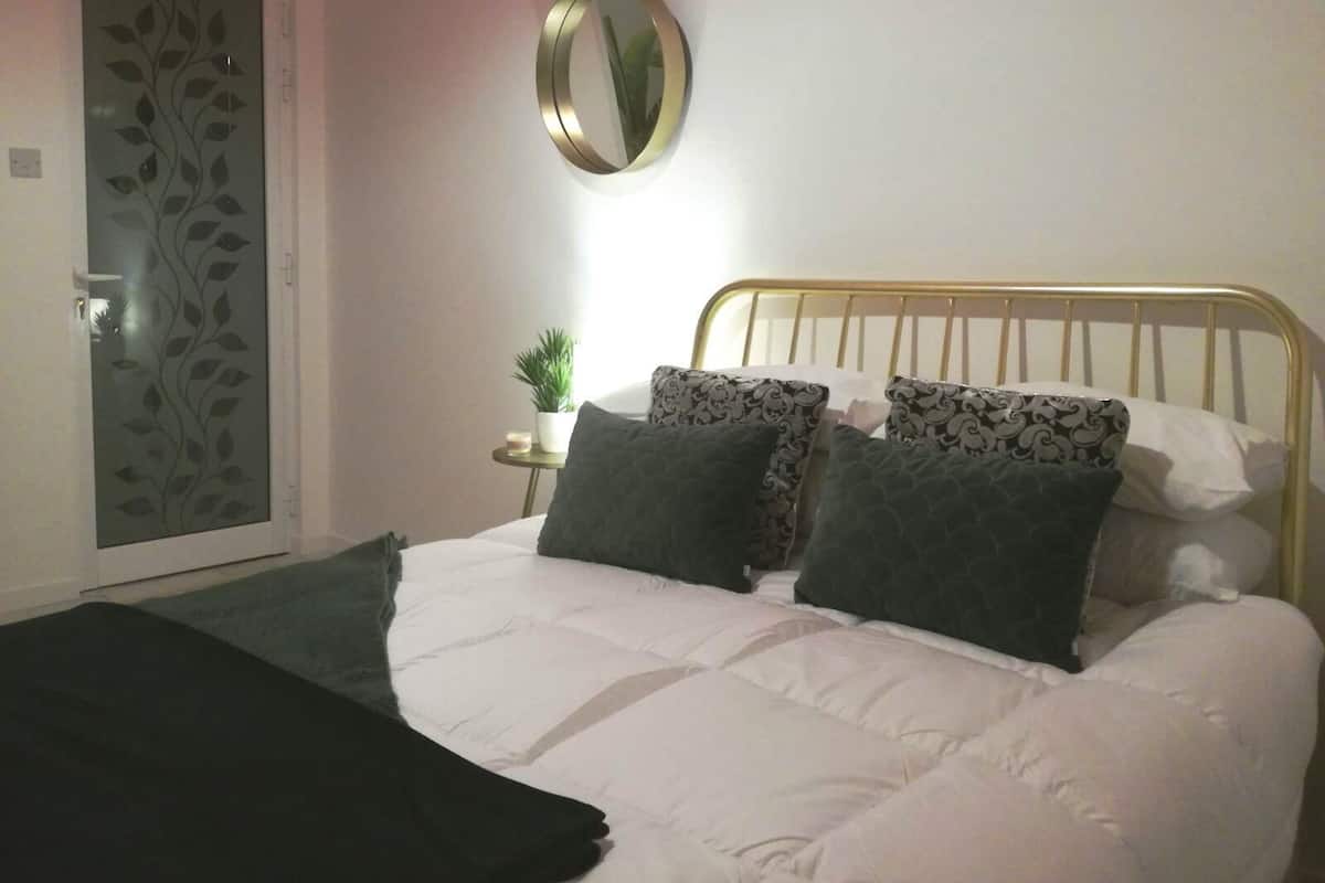 A bedroom with a bed, a round mirror, a small table with a plant, and a door with a leaf pattern.