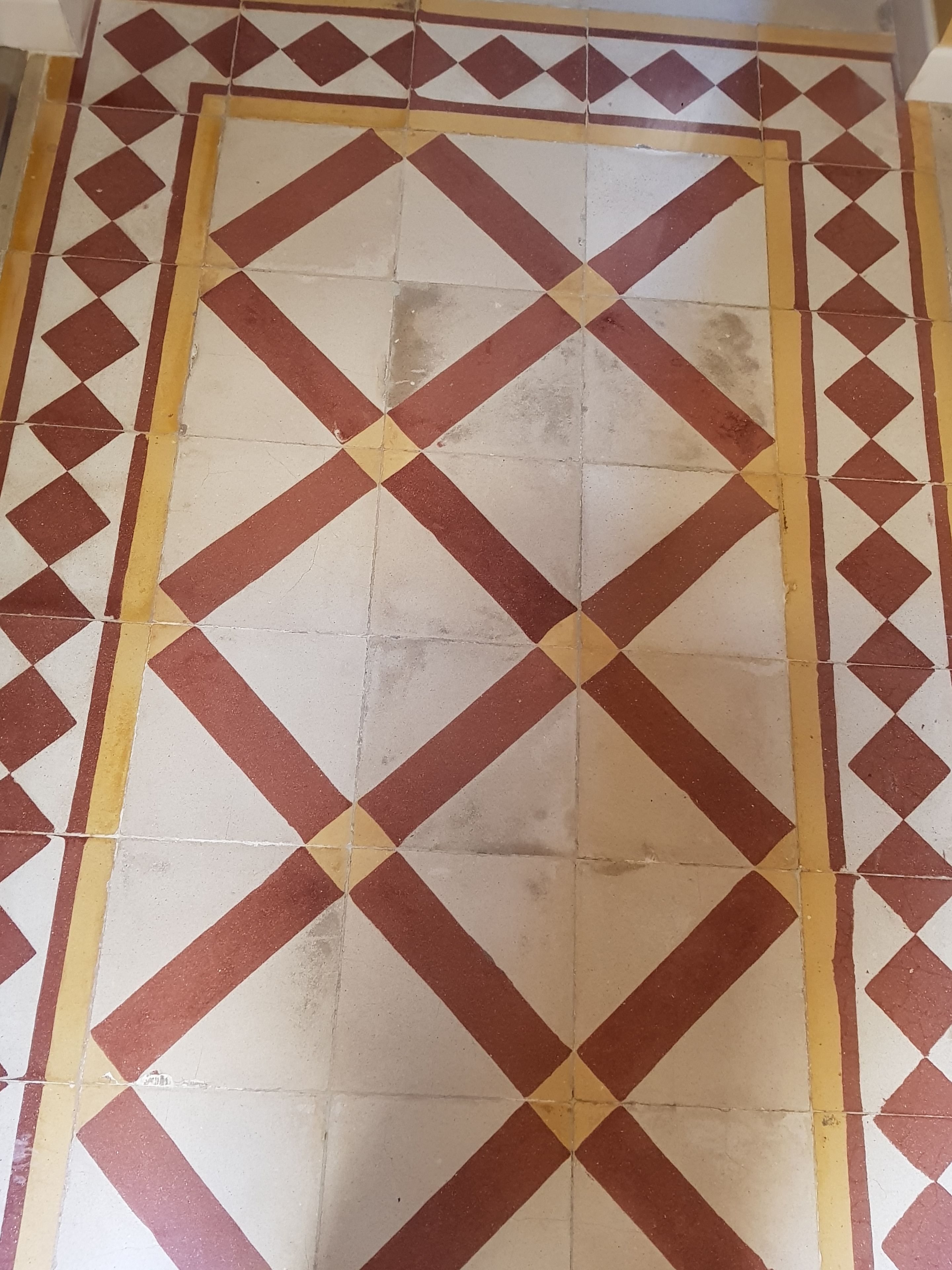 Un sol carrelé orné d’un motif g éométrique composé de carreaux rouges et blancs, bordé de lignes jaunes.