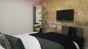 Un dormitorio con cama, televisor montado en una pared de ladrillo y espejo.