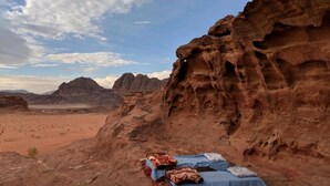 A desert landscape with a rocky outcrop and a bed set up on a patterned rug. - Mars Private camp (Wadi Rum)