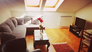A living room with a sofa, a coffee table with a vase, a television, and a red rug. - Apartments Patricija (Opatija)
