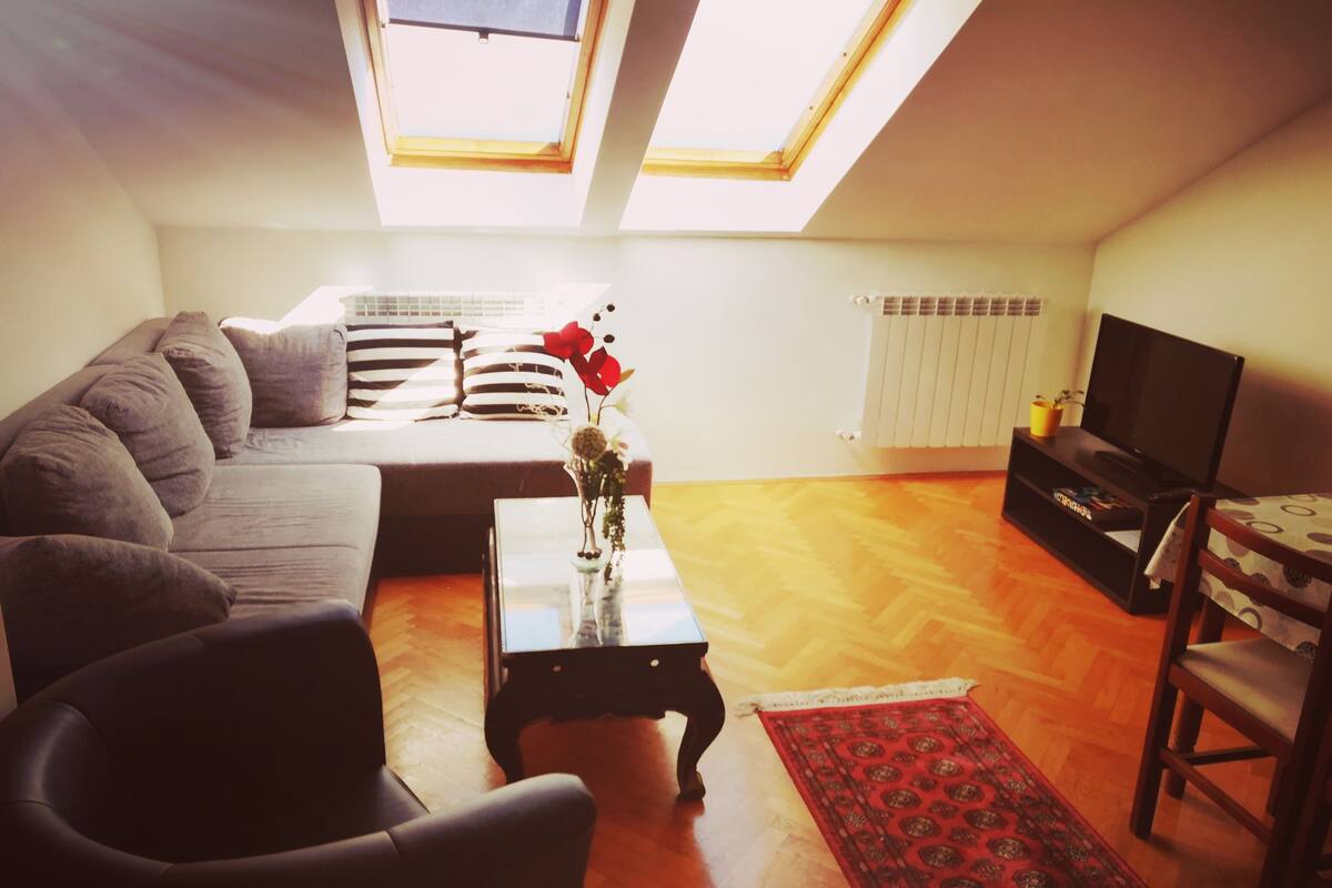 A living room with a sofa, a coffee table with a vase, a television, and a red rug.