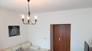 A living room with a sofa, a small table, a TV, and a wooden door. - Apartments Patricija (Opatija)