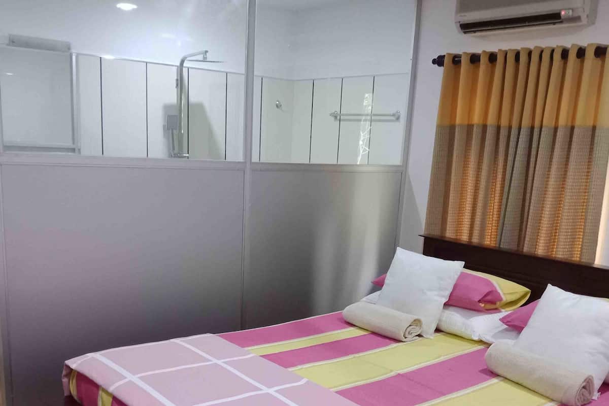 A hotel room with a bed, a shower area, and a window with curtains.