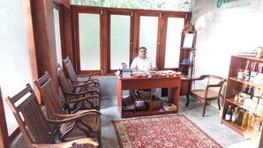 A room with wooden furniture, a red patterned rug, and a shelf with bottles. - Himana Ayurveda (Seeduwa - Katunayake)