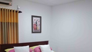 A hotel room with a bed, pillows, a framed picture on the wall, and an air conditioning unit. - Himana Ayurveda (Seeduwa - Katunayake)