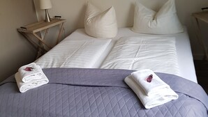 Una cama bien hecha con una colcha gris acolchada, dos toallas blancas y un cuadro en la pared.