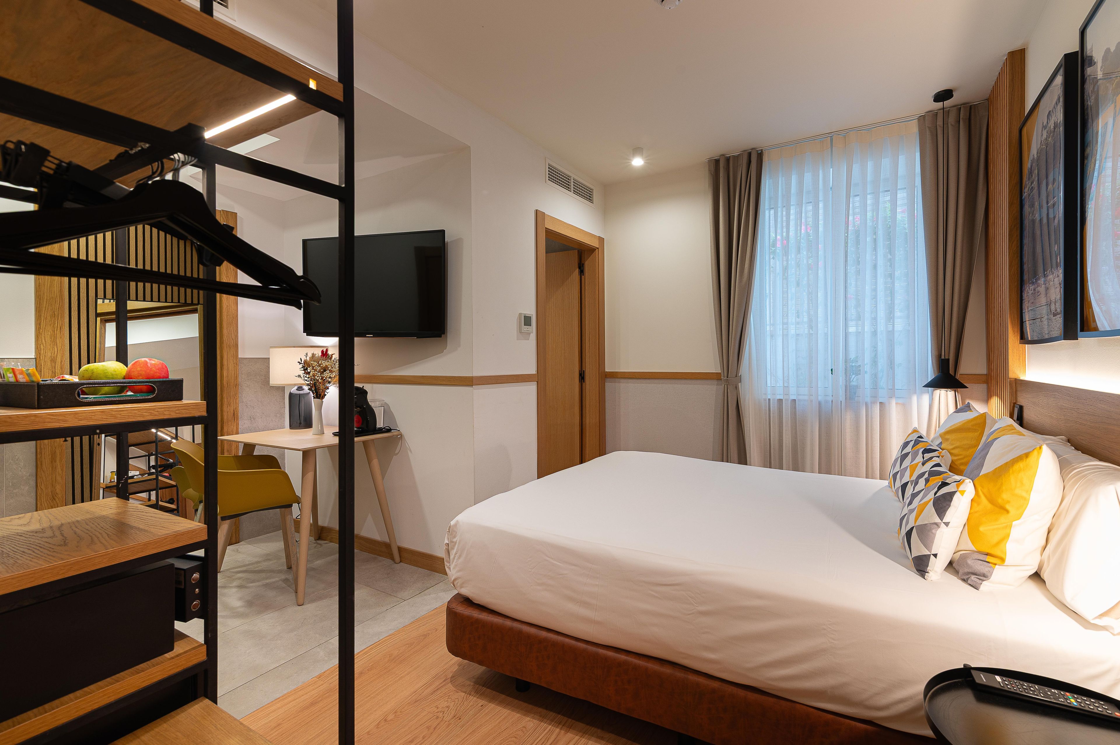 Habitación de hotel con cama, escritorio, silla, televisor y armario.