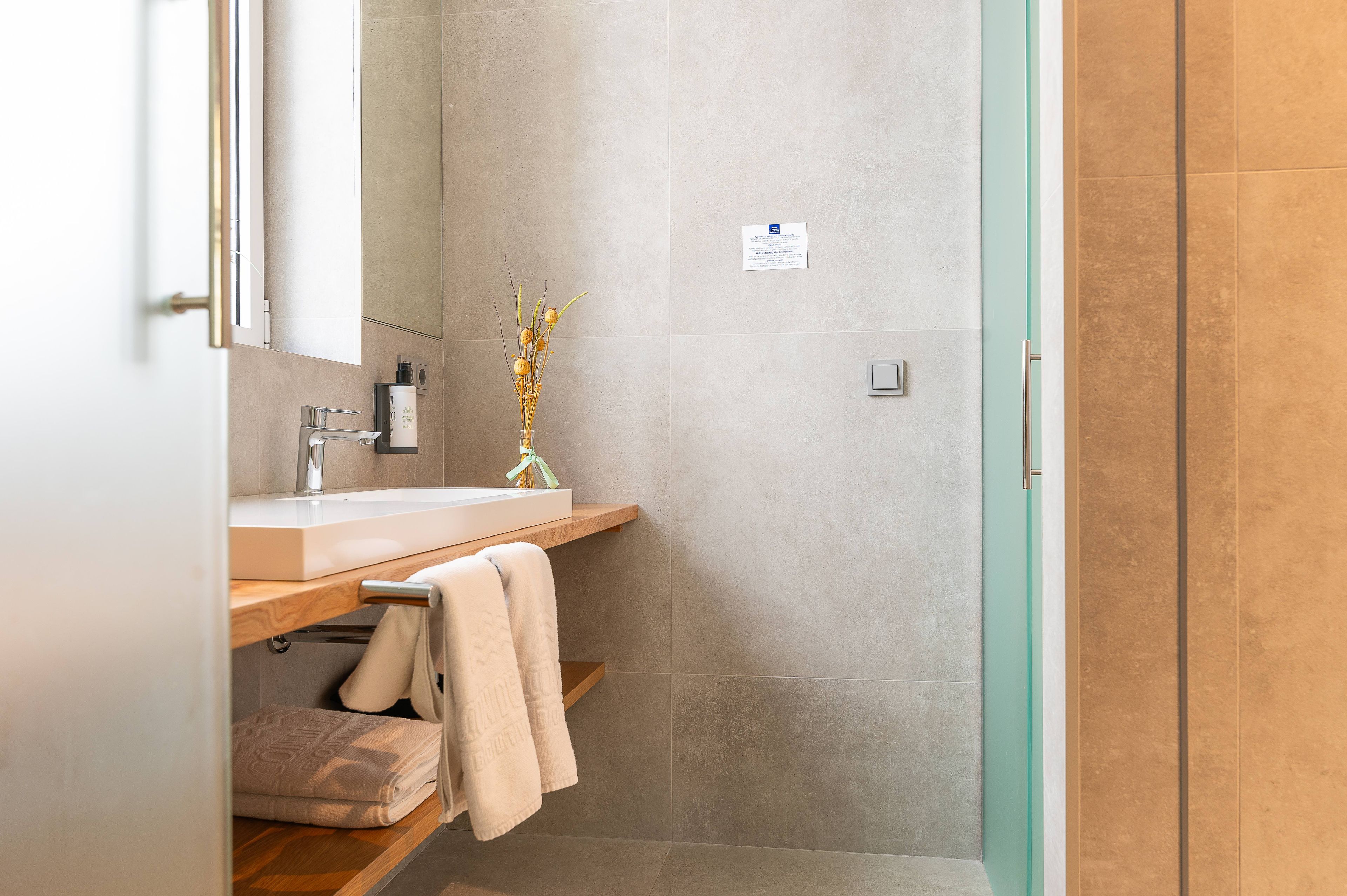 Un baño moderno con lavamanos, espejo, toallero y zona de ducha.
