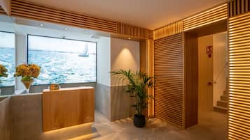 A reception area with a view of the sea, a reception desk, a potted plant, and a staircase.
