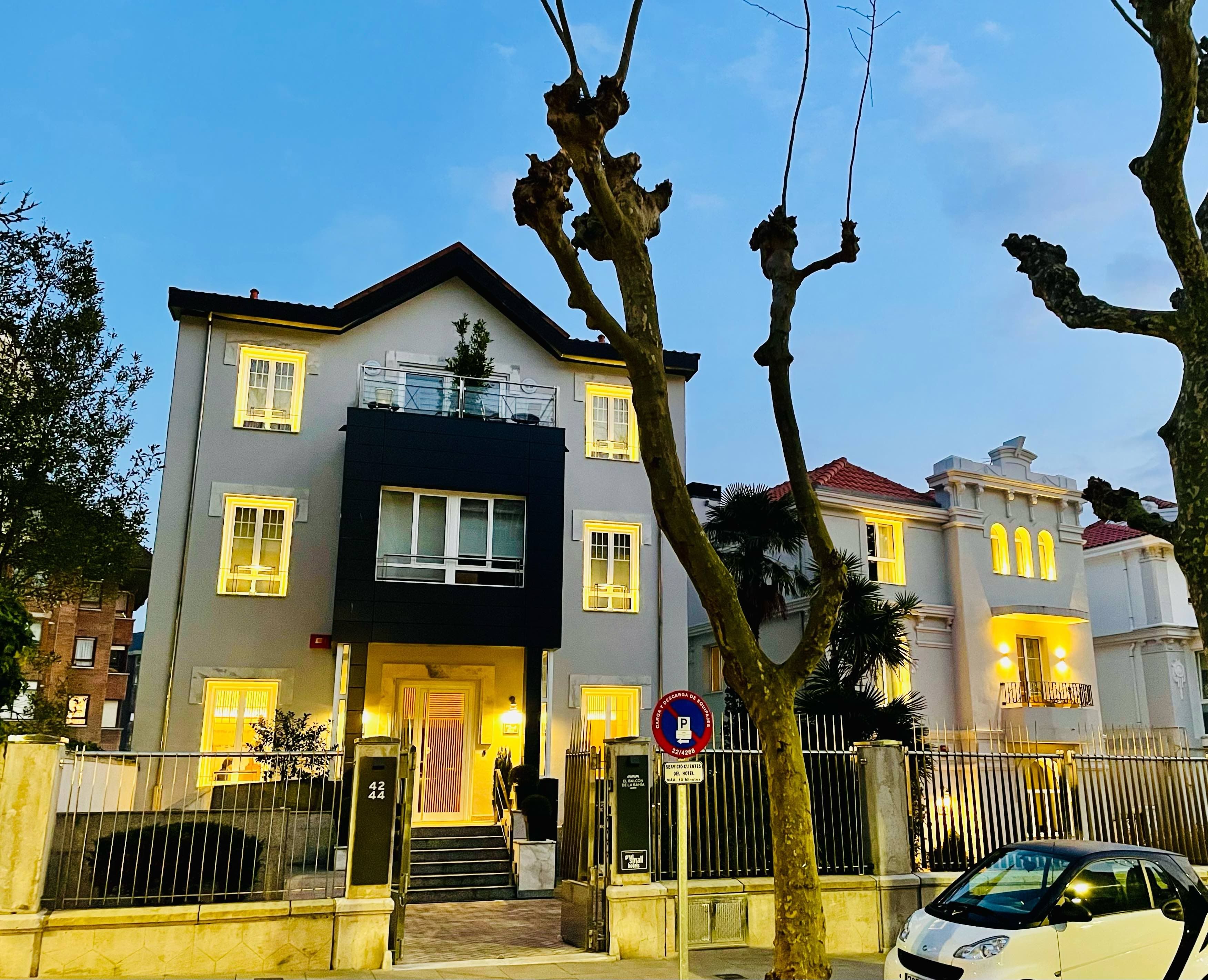 A multi-story hotel with a central entrance, a balcony on the upper floor, and a gated driveway.