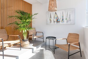 Un interior moderno con mobiliario de mimbre, una planta en maceta y un cuadro de un velero.