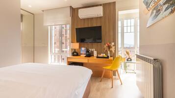 Habitación de hotel con cama, escritorio con silla, televisor y ventana con vista a la ciudad.