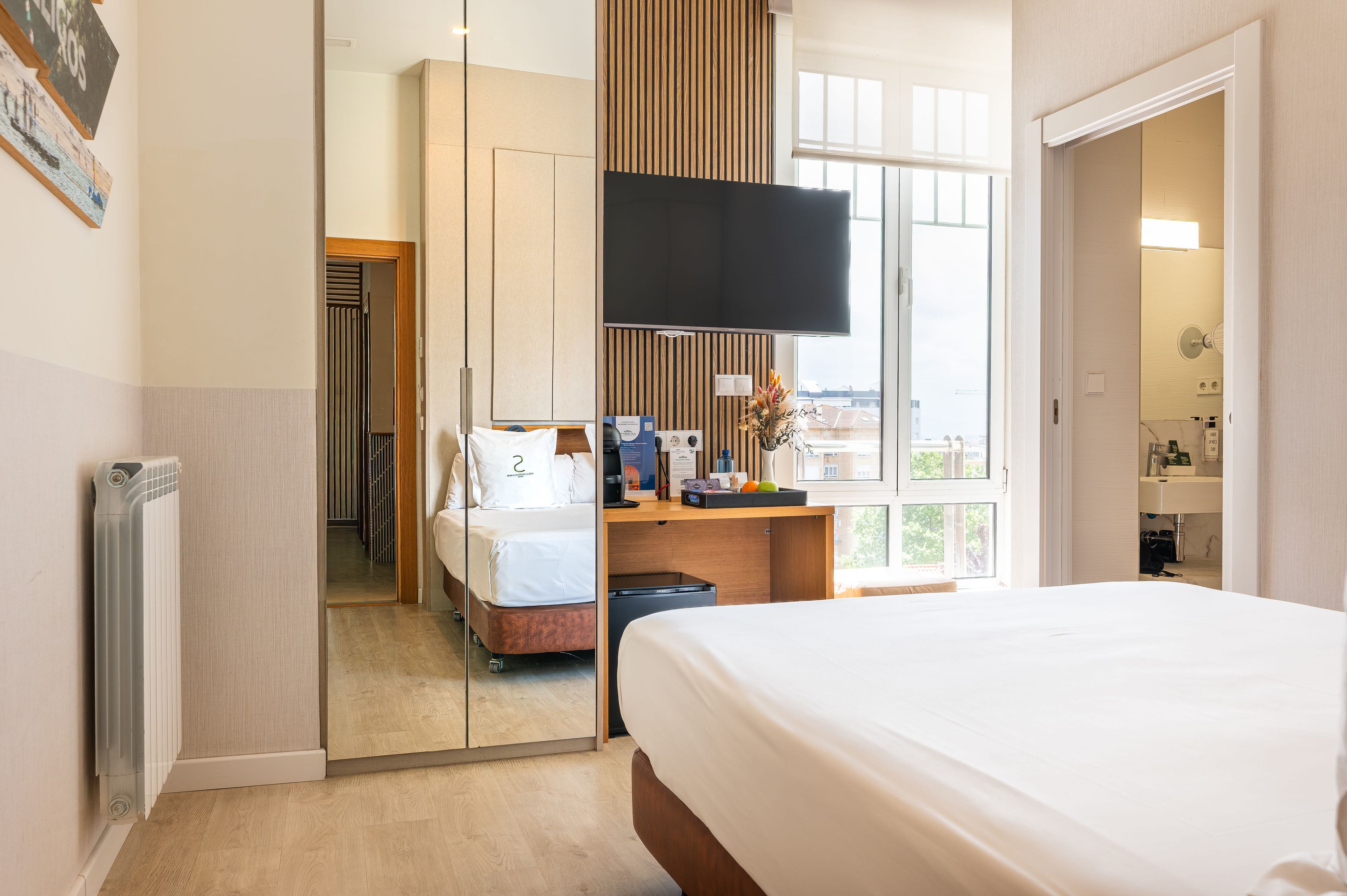 Habitación de hotel con cama, escritorio, televisión, espejo y vistas al exterior.