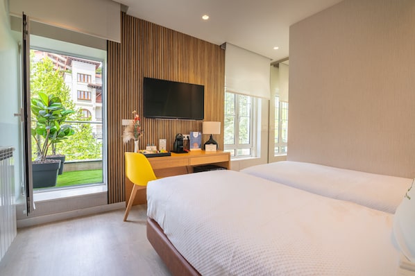 Habitación de hotel con cama, escritorio con silla, televisor de pantalla plana y ventana con vistas a edificios y zonas verdes.