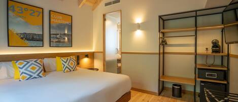 A hotel room with a bed, a desk with shelves, a chair, and a wall-mounted light.