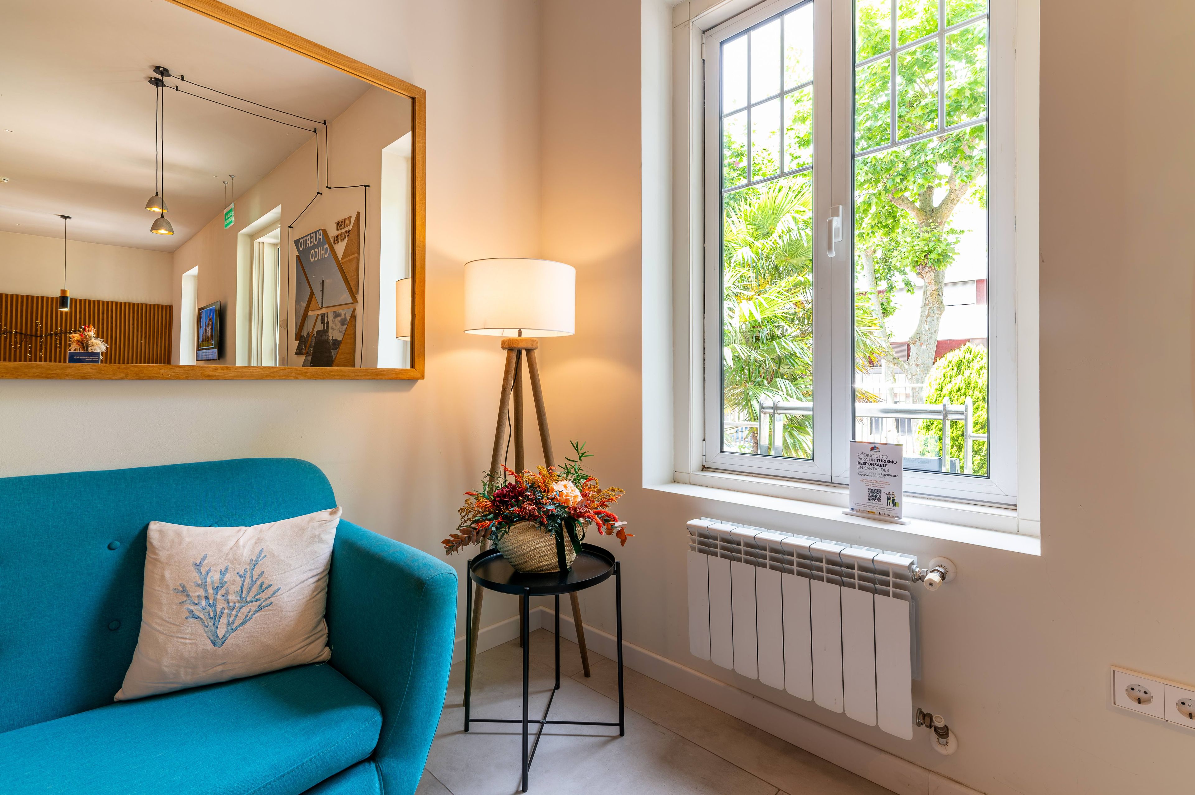 A room with a blue sofa, a floor lamp, a mirror, and a window with a view of trees.