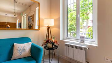 A room with a blue sofa, a floor lamp, a mirror, and a window with a view of trees.