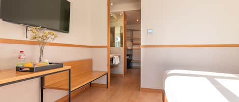 A hotel room with a bed, a desk with a chair, a television mounted on the wall, and a small table with a vase of flowers.